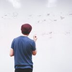 man standing while holding red marker pen facing marker board