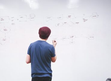 man standing while holding red marker pen facing marker board